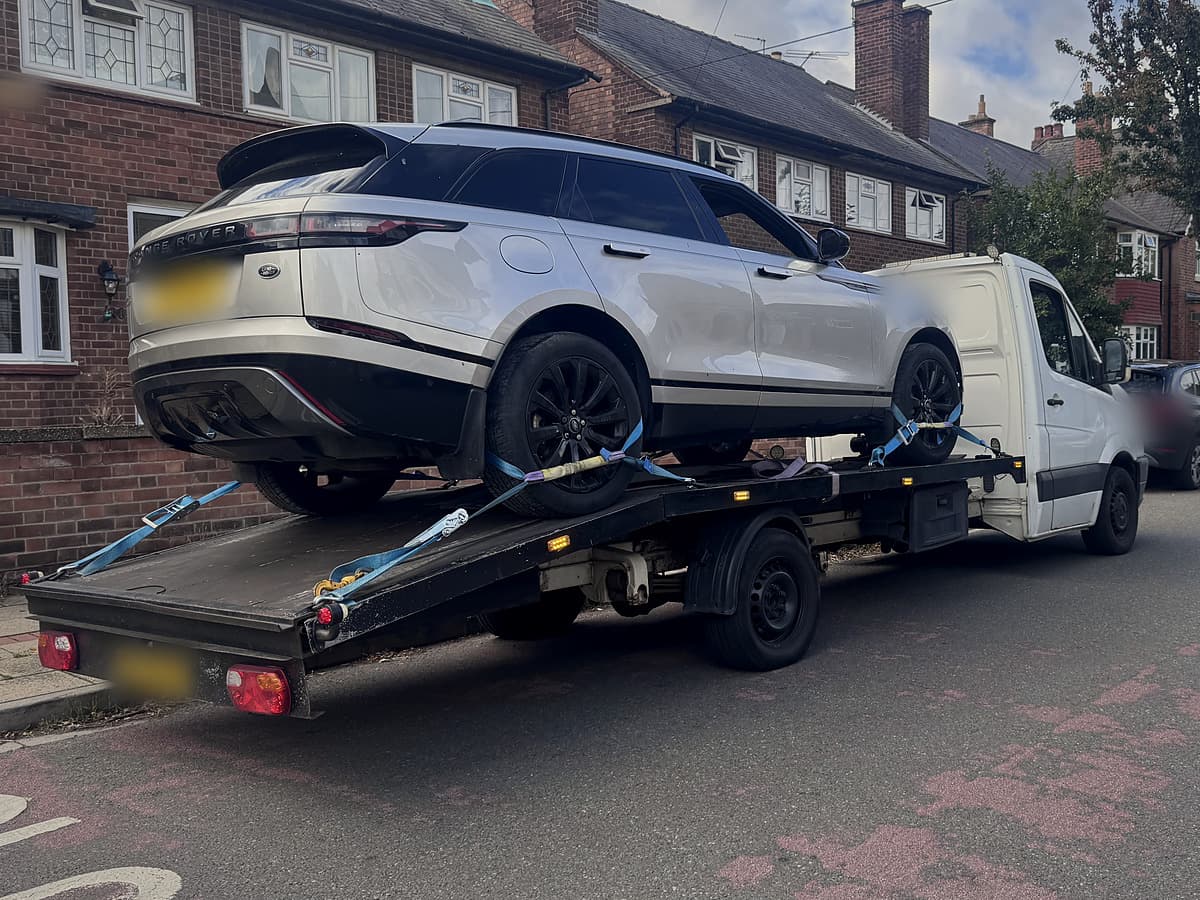 A silver Range Rover strapped onto the flatbed of a recovery truck in a residential street